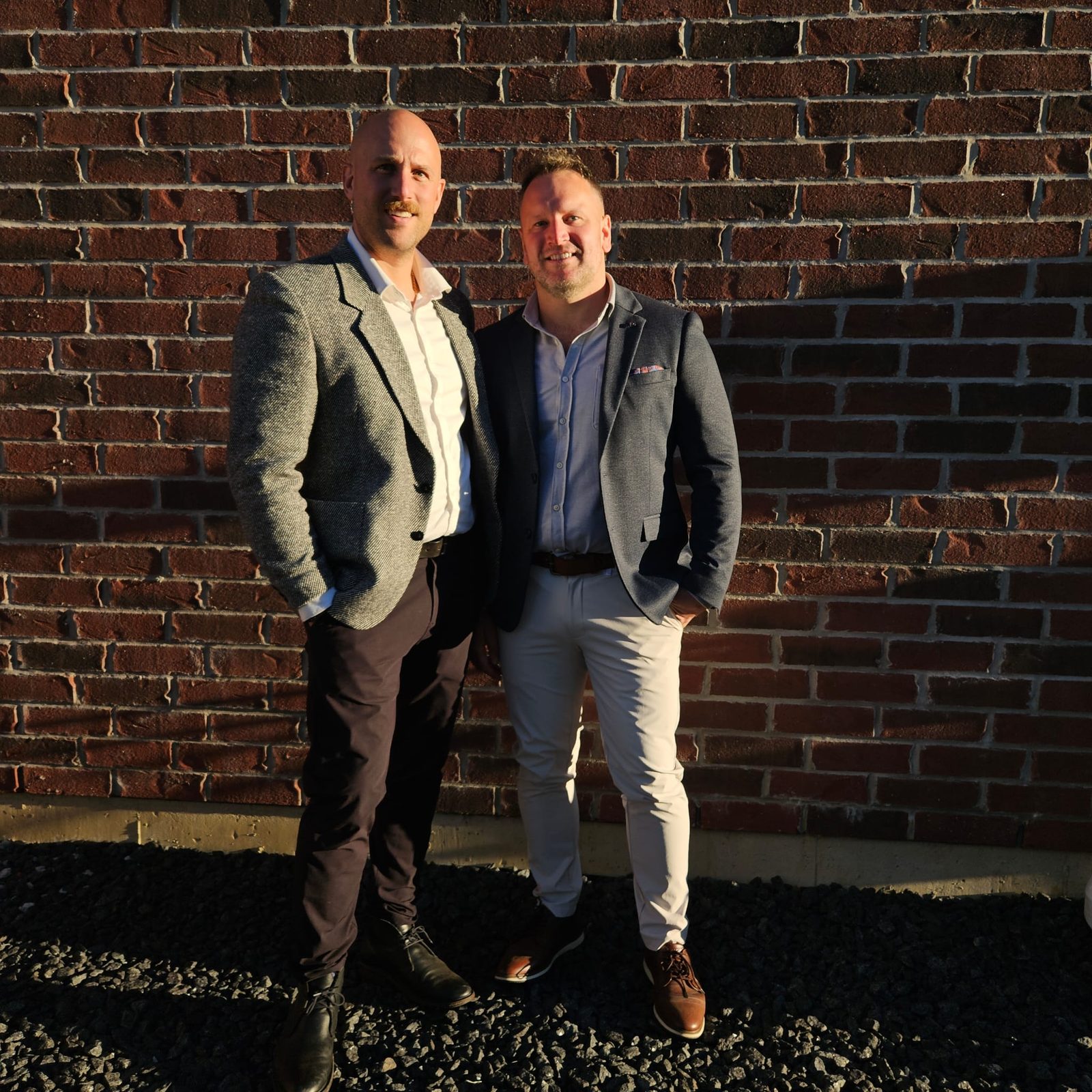 The duo in front of a brick wall at sunset